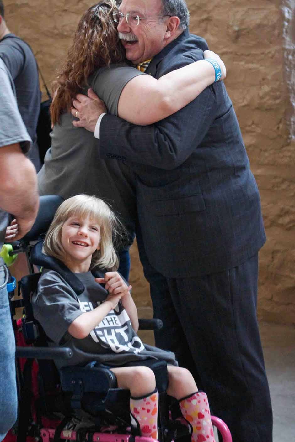 Loftin hugging a woman next to a smilig girl in a wheelchair.