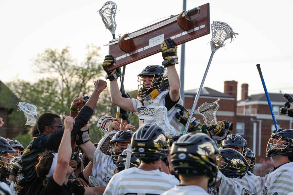 A Mizzou lacrosse player holds the Civil War sword above his head while on the shoulders of his teammates.