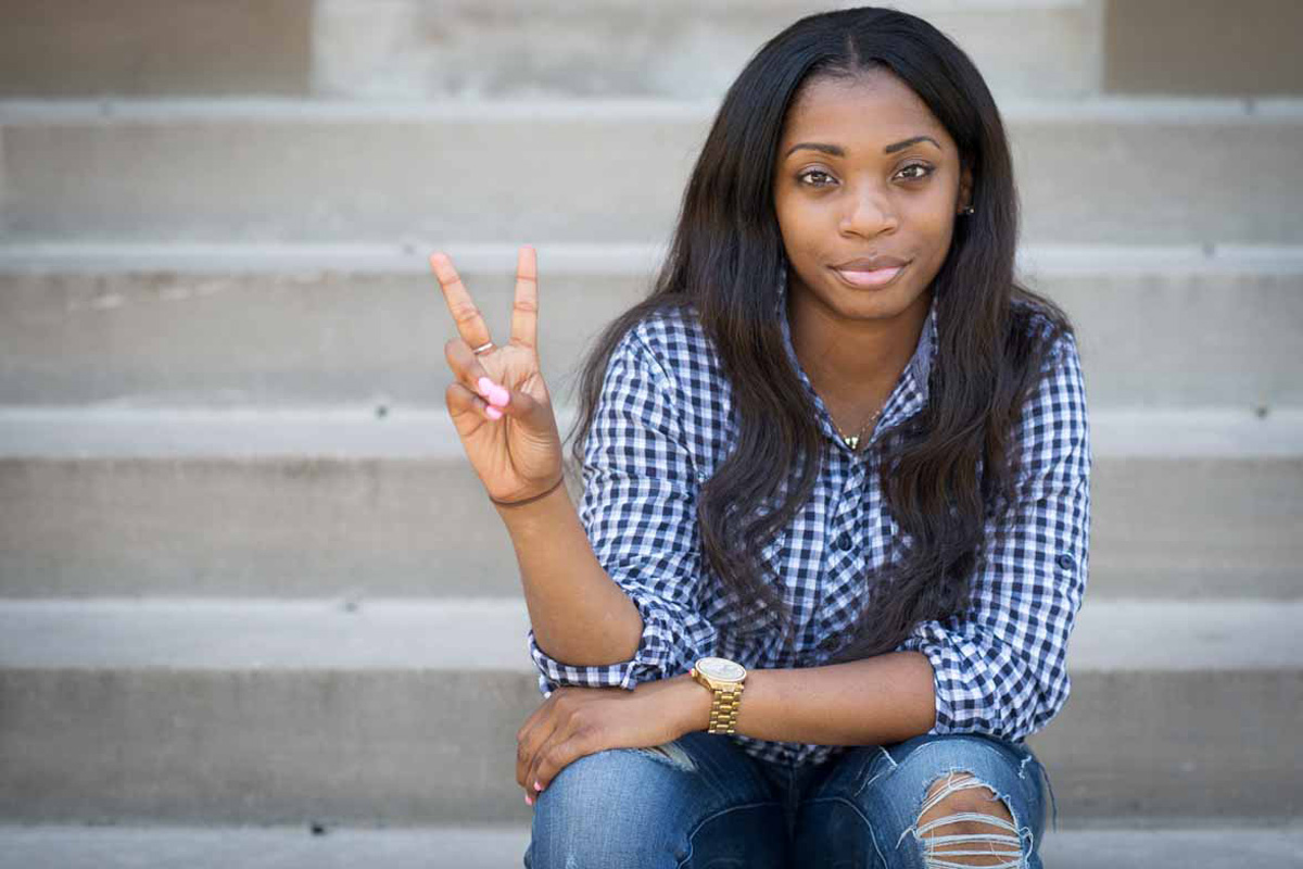 Razia Hutchins on the steps of Jesse Hall making a peace sign with her right hand.