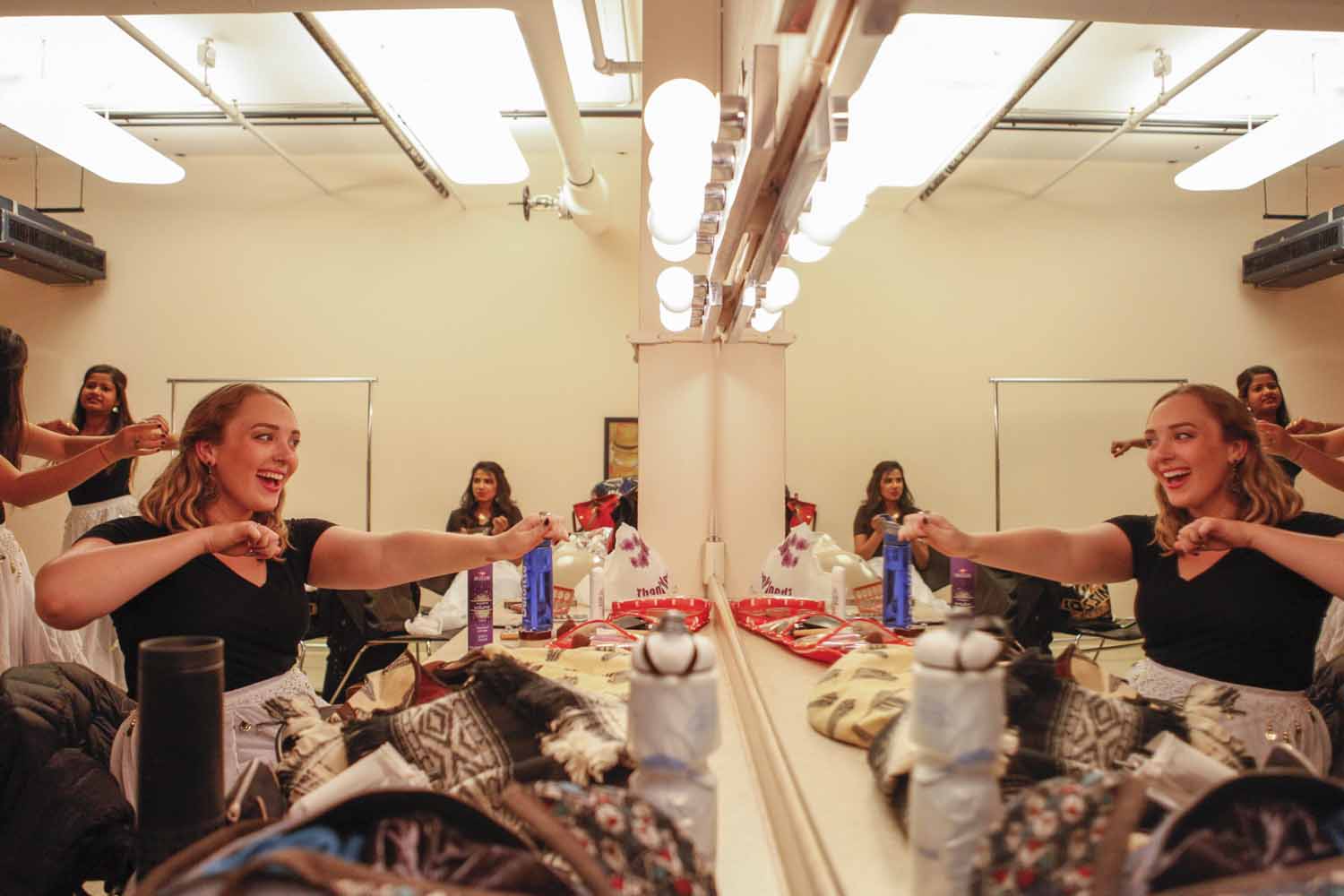 Kelsey Burns practices arm movements to her group's upcoming performance in the mirror of a dressing room in Jesse Hall as the rest of the ensembe dances around the room.