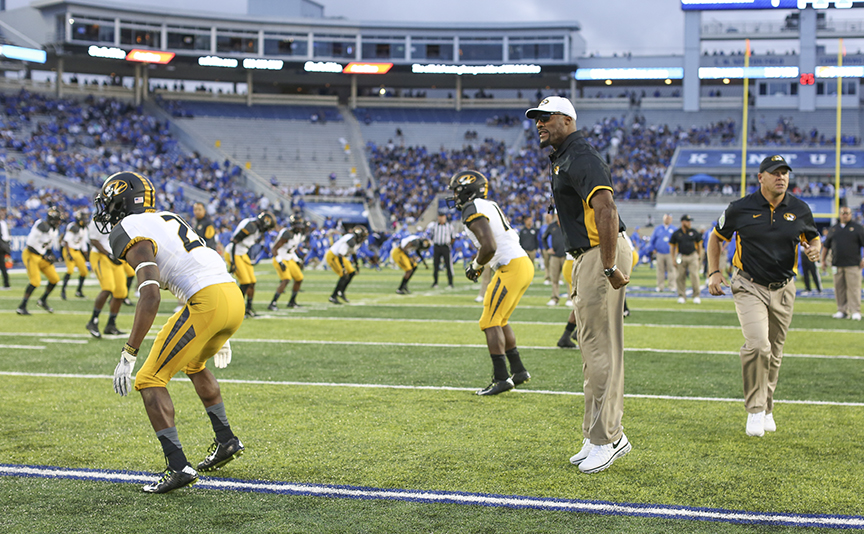 Coach and players warm up on football field.