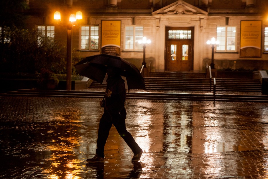 Student walking in the rain at night with an umbrella.