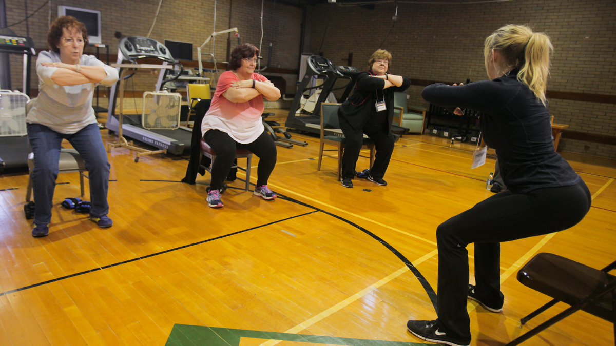 People in chair pose in a gym.