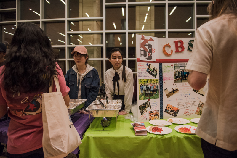 Students at a table with Chinese food and a poster display.