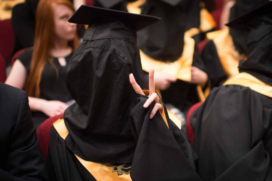 Although her vision is almost blinded by a black hood, a member of Mortar Board flashes a peace sign.