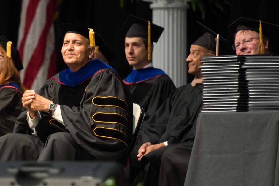Dean seated next to stack of diplomas.