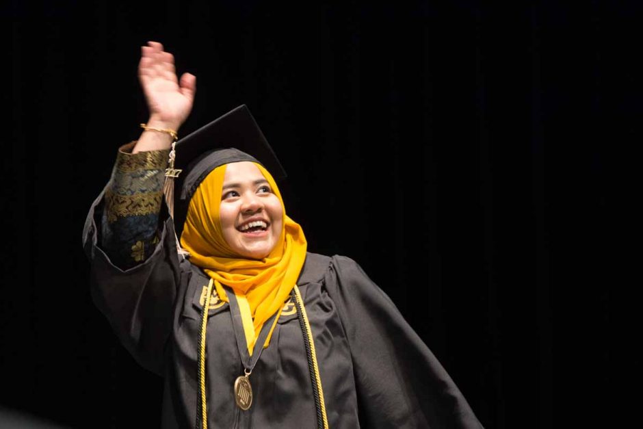 Woman in cap and gown and gold head scarf.