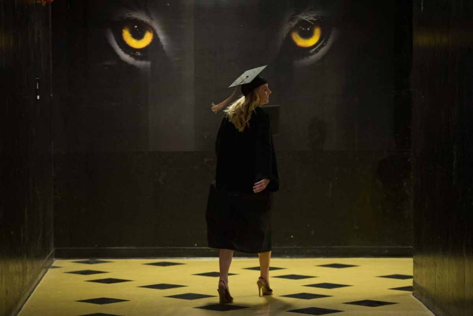 Woman in cap and gown walking in front of tiger eyes.