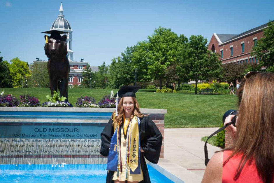 Woman in cap and gown in front of the fountain.
