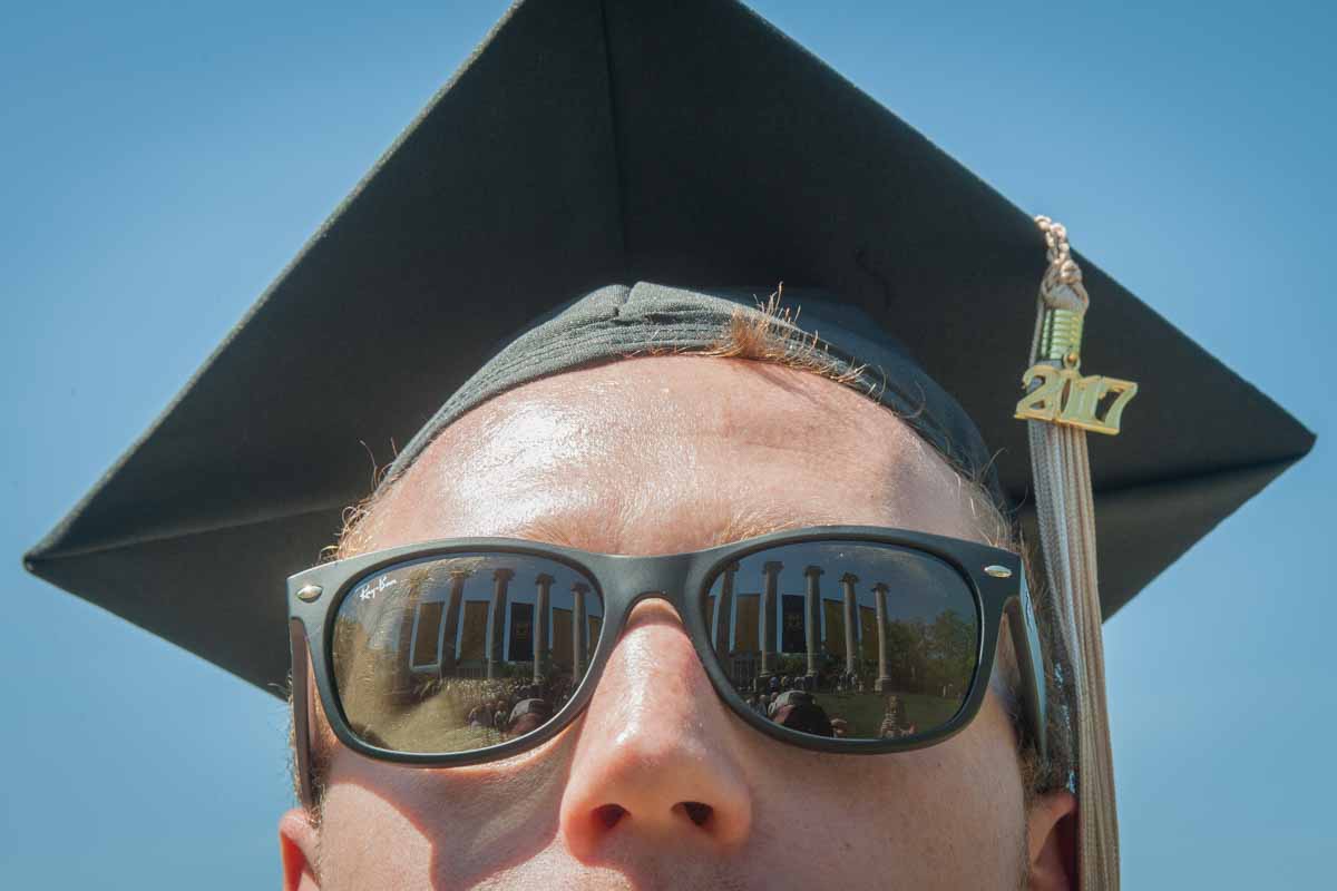 Student in cap and gown with columns reflected in sunglasses.