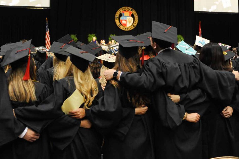 Students in caps and gowns with arms around each other.
