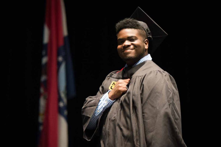 A journalism graduate celebrates on stage by placing his fist on his heart. Photo by Shane Epping.