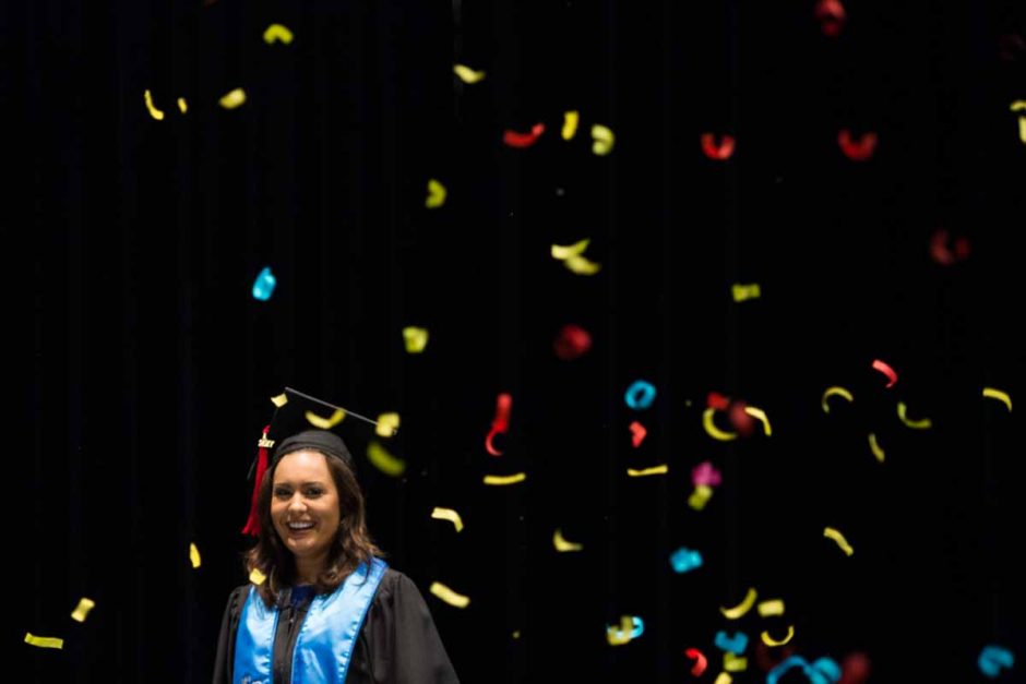 Woman in cap and gown surrounded by confetti.