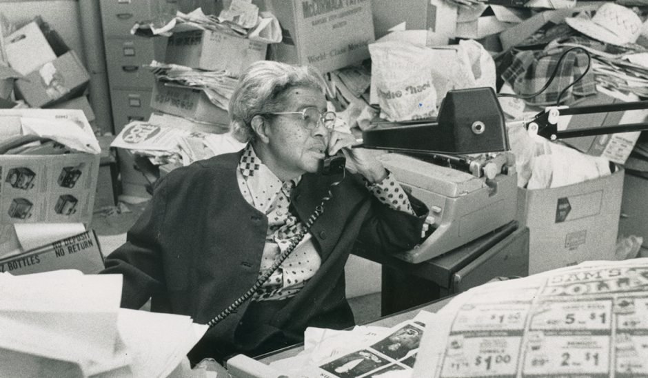 Lucille Bluford sits at her desk speaking on the phone.