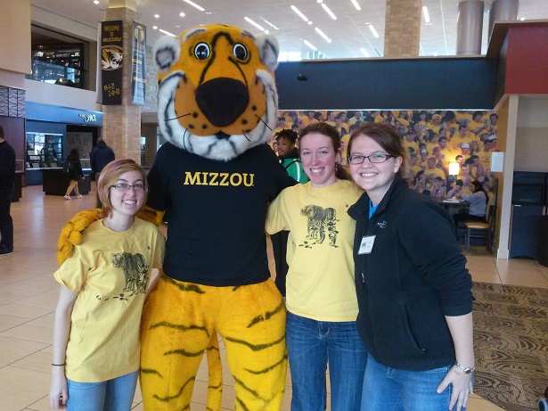 Three students stand with their arms around each other and the Mizzou mascot, Truman the Tiger