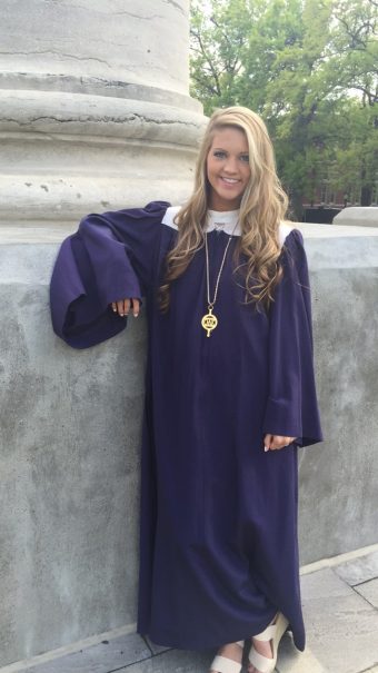 Libby Martin in a graduation cap and gown leaning against one of the Columns.