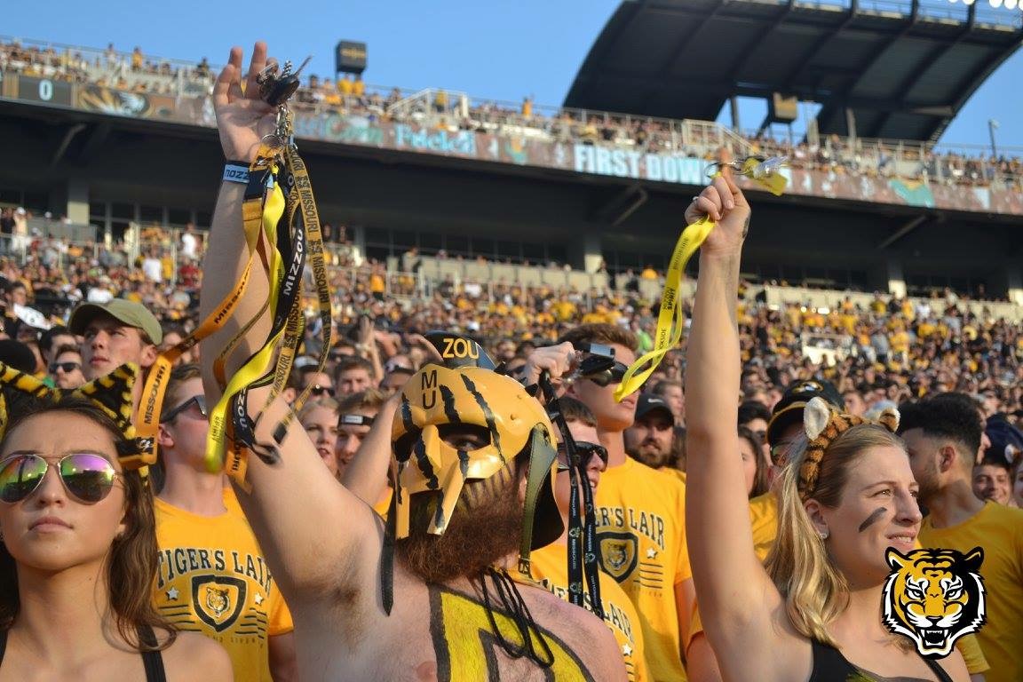 Picture of Truman Kinsey in the student section at Faurot, Kinsey is wearing a black and gold face mask and body paint and is dangling keys for the third down. 